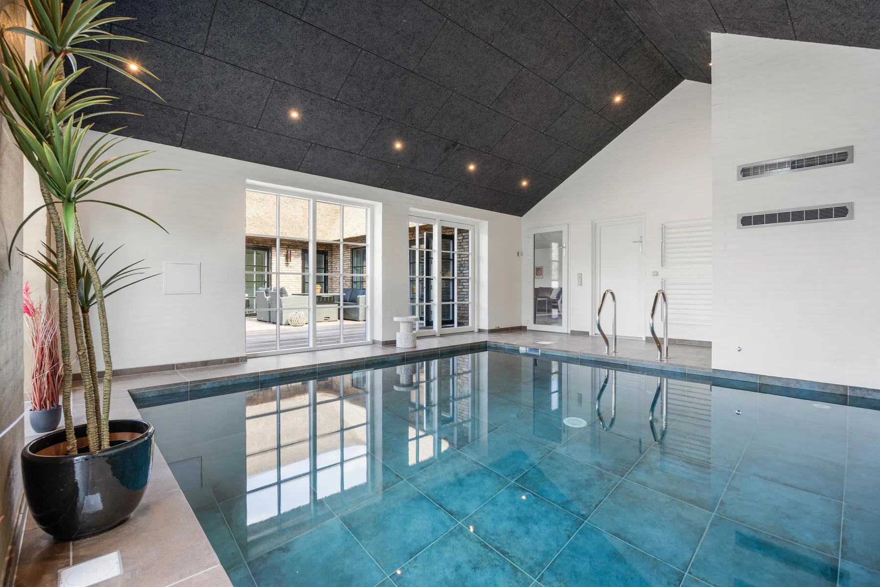 An indoor swimming pool reflects the large windows and dark ceiling.