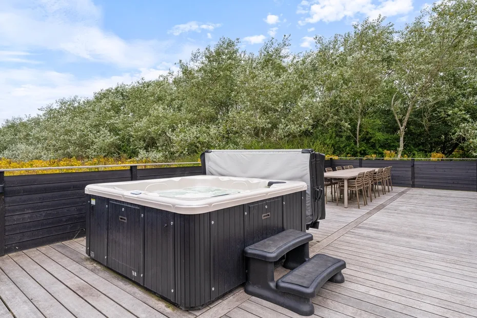 An outdoor hot tub sits on a wooden deck beside a dining table.