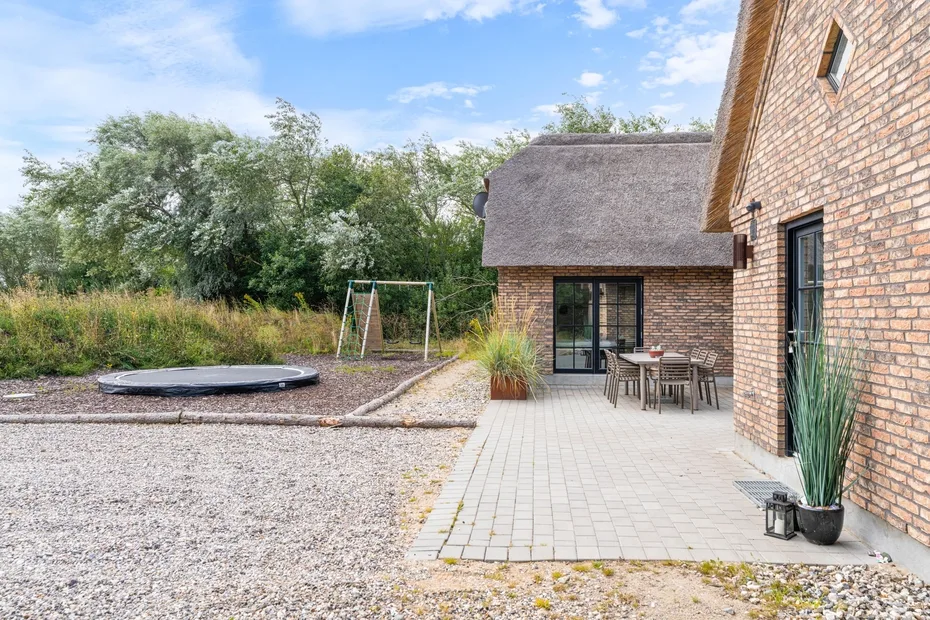 A brick house opens onto a paved patio with outdoor seating and a garden.