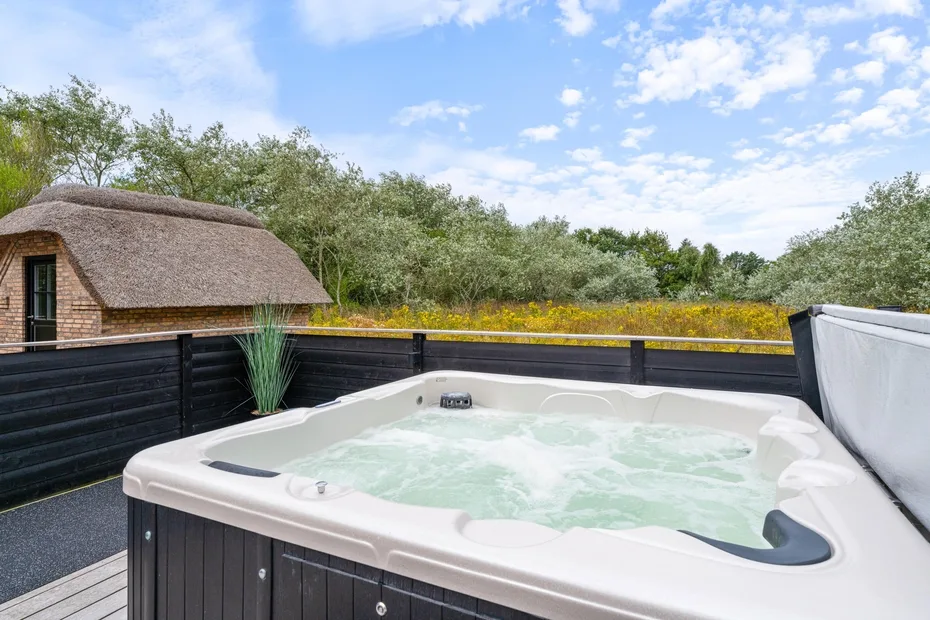 An outdoor hot tub sits on a raised deck beside a dark fence.