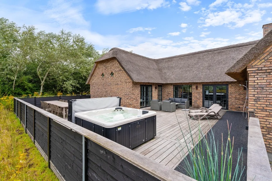 A brick house opens onto a deck with a hot tub and outdoor seating.