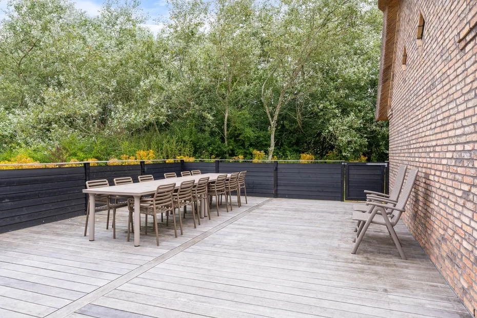 An outdoor deck with a long dining table and seating beside a brick wall.