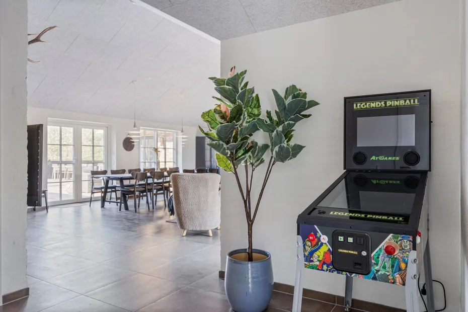 A bright dining and game area features a table, seating, and a pinball machine.