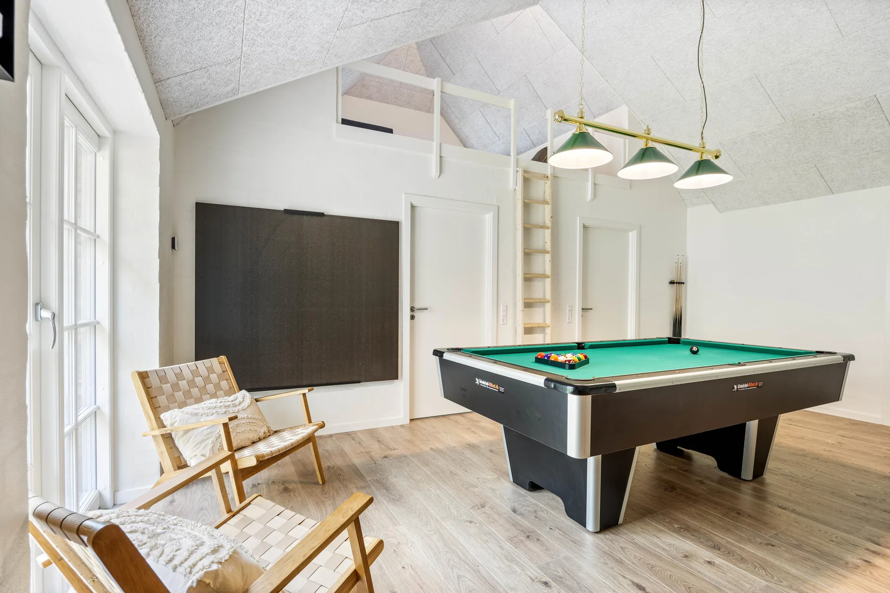 A bright game room with a pool table and seating by the windows.