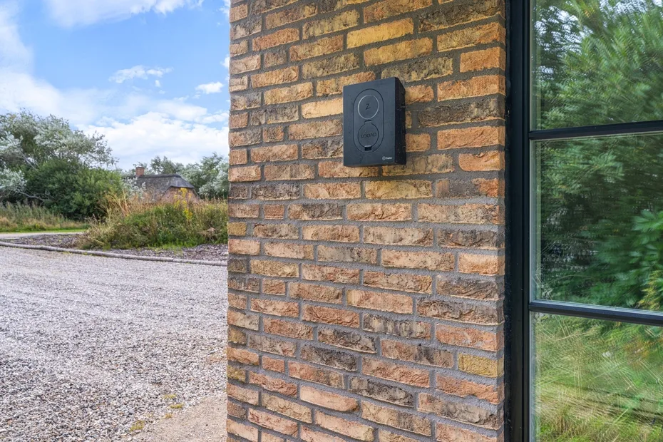 A brick exterior wall with a mounted doorbell beside a large window.