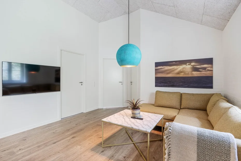 A bright living room with beige seating, a coffee table, and a turquoise pendant light.