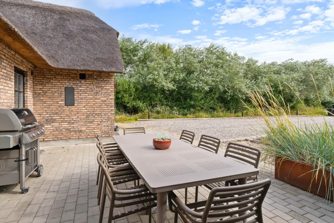 An outdoor dining area with a long table and seating beside a brick building.
