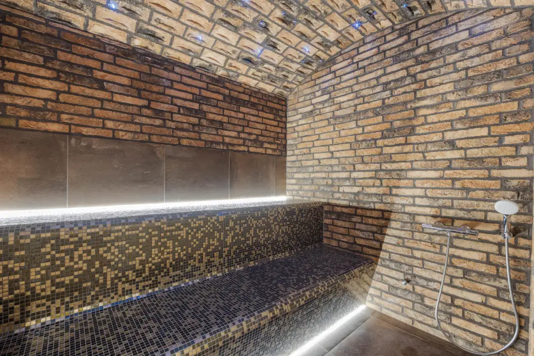A tiled steam room with a long built-in bench and a handheld shower.