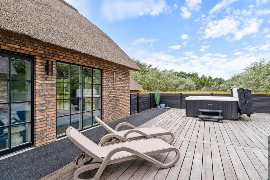 A wooden deck beside a brick house has lounge seating and a hot tub.