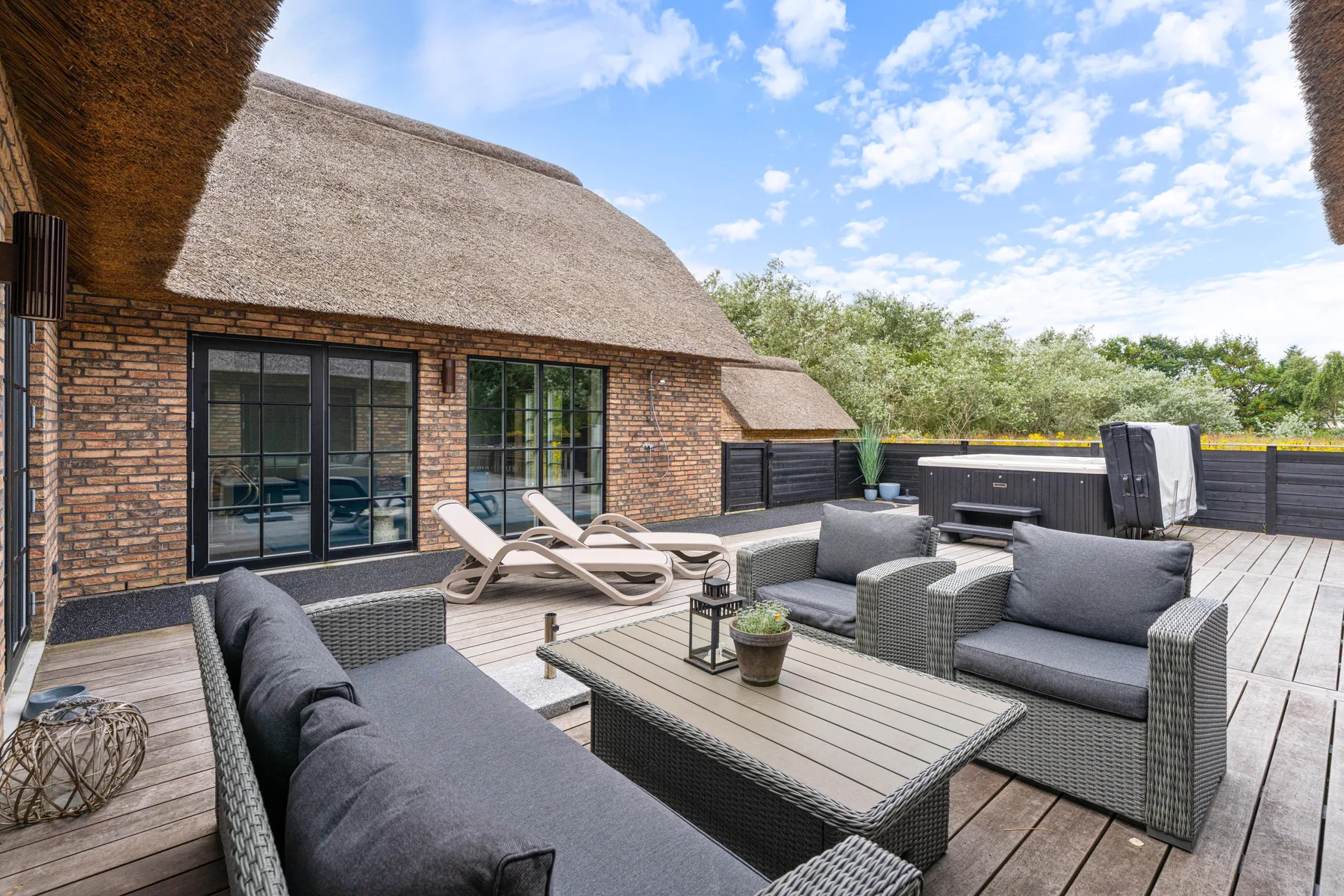 An outdoor deck seating area with cushioned seating and a low table beside a brick house.