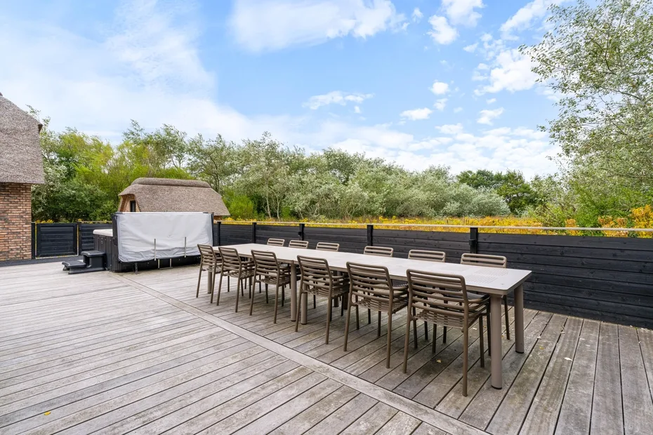 An outdoor dining area with a long table and seating on a wooden deck.