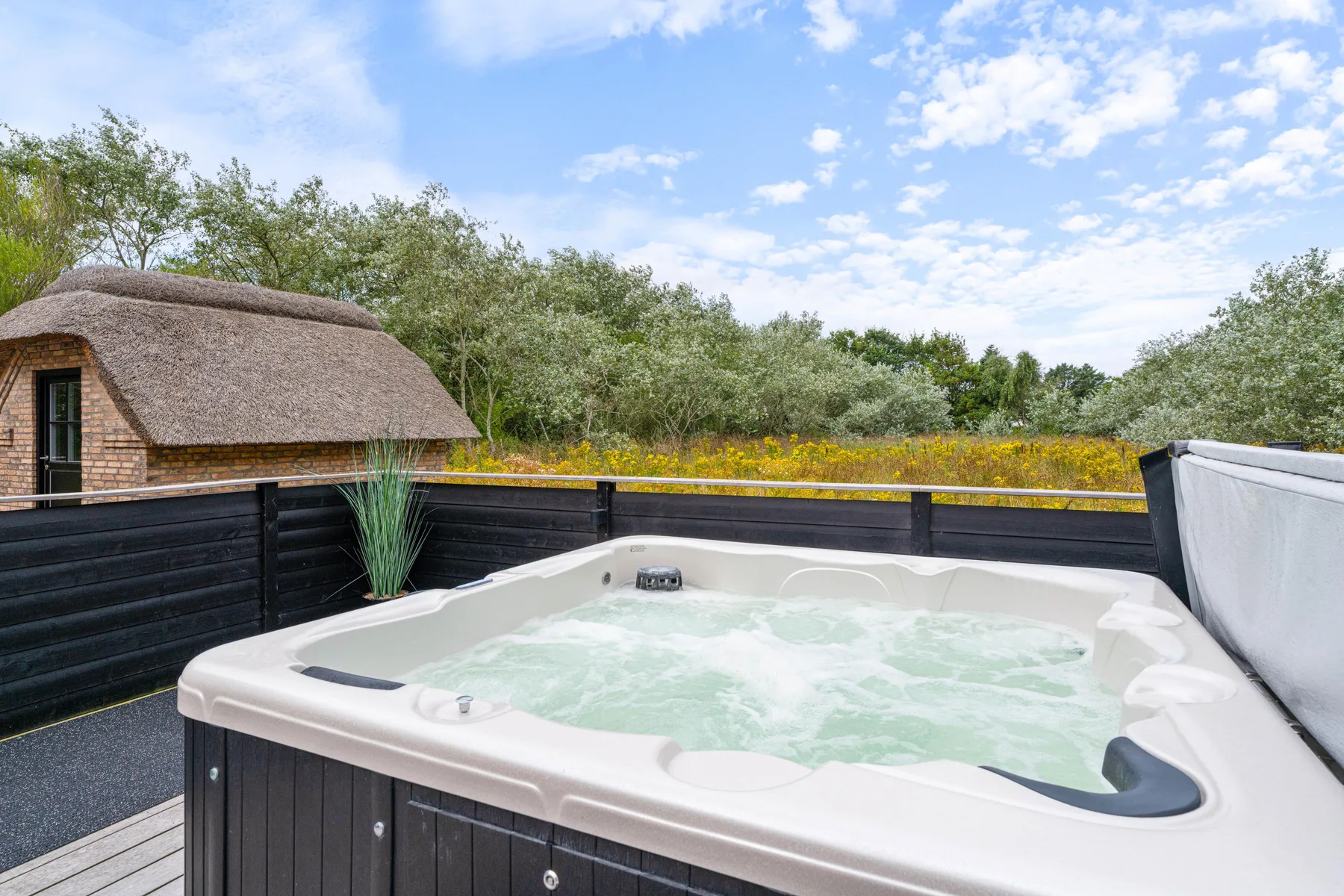 An outdoor hot tub sits on a deck beside a dark wooden fence.