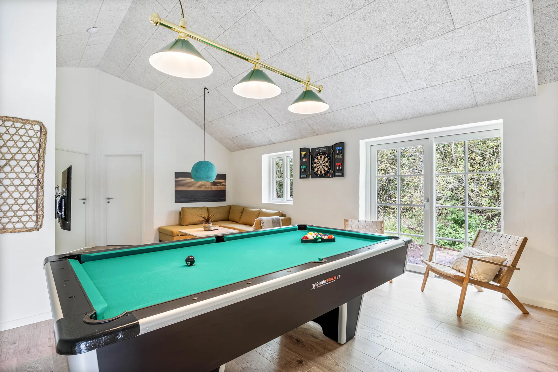 A game room features a pool table, wall-mounted dartboard, and large windows.
