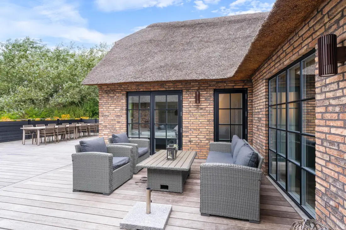 A brick house opens onto a wooden patio with outdoor seating.
