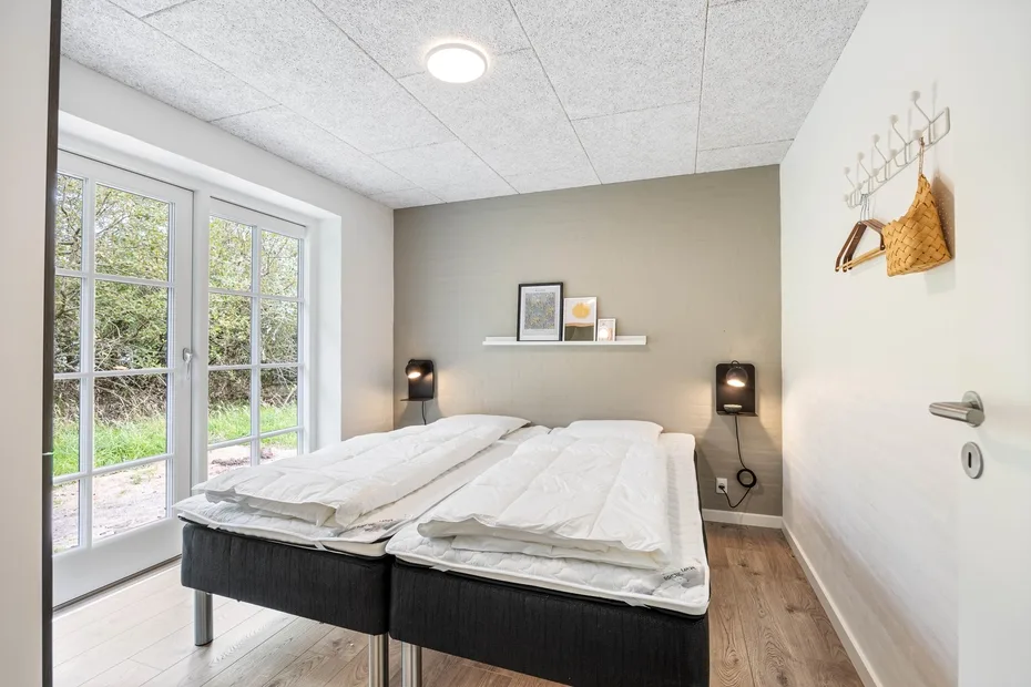 A bedroom with two beds beside large glass doors overlooking greenery.