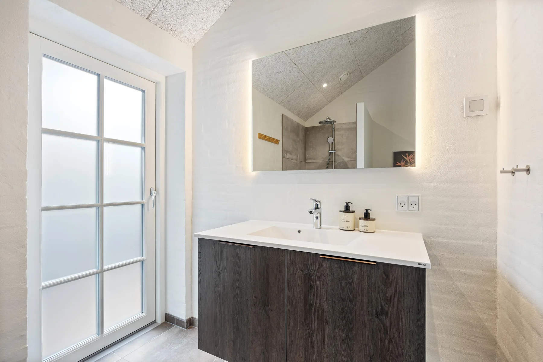 A bright bathroom with a sink vanity, large mirror, and frosted glass door.