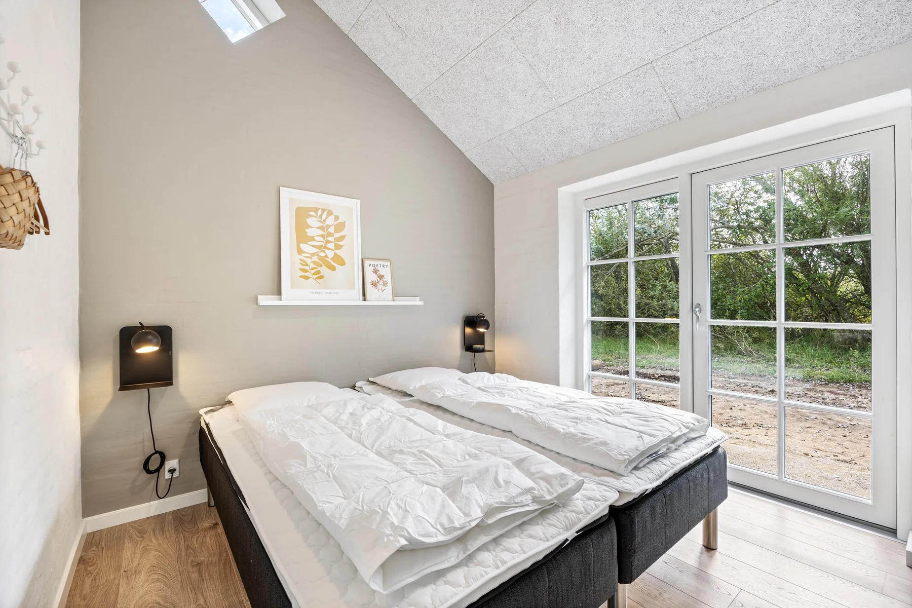 A bright bedroom with two beds beside large glass doors overlooking greenery.