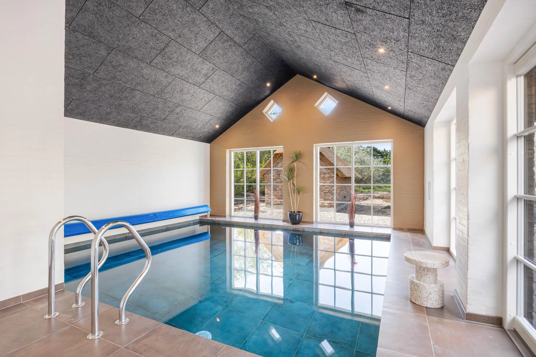 An indoor swimming pool with large windows and a high sloped ceiling.