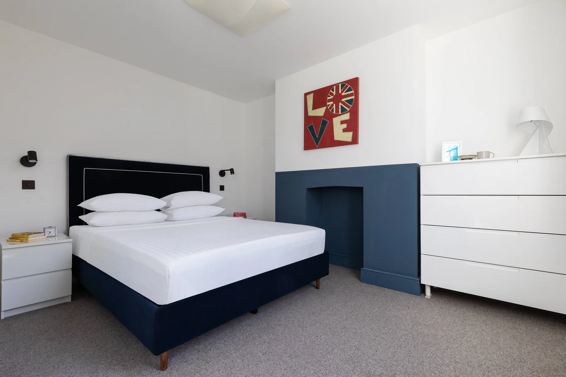 A bedroom with a neatly made bed and a dark blue fireplace surround.