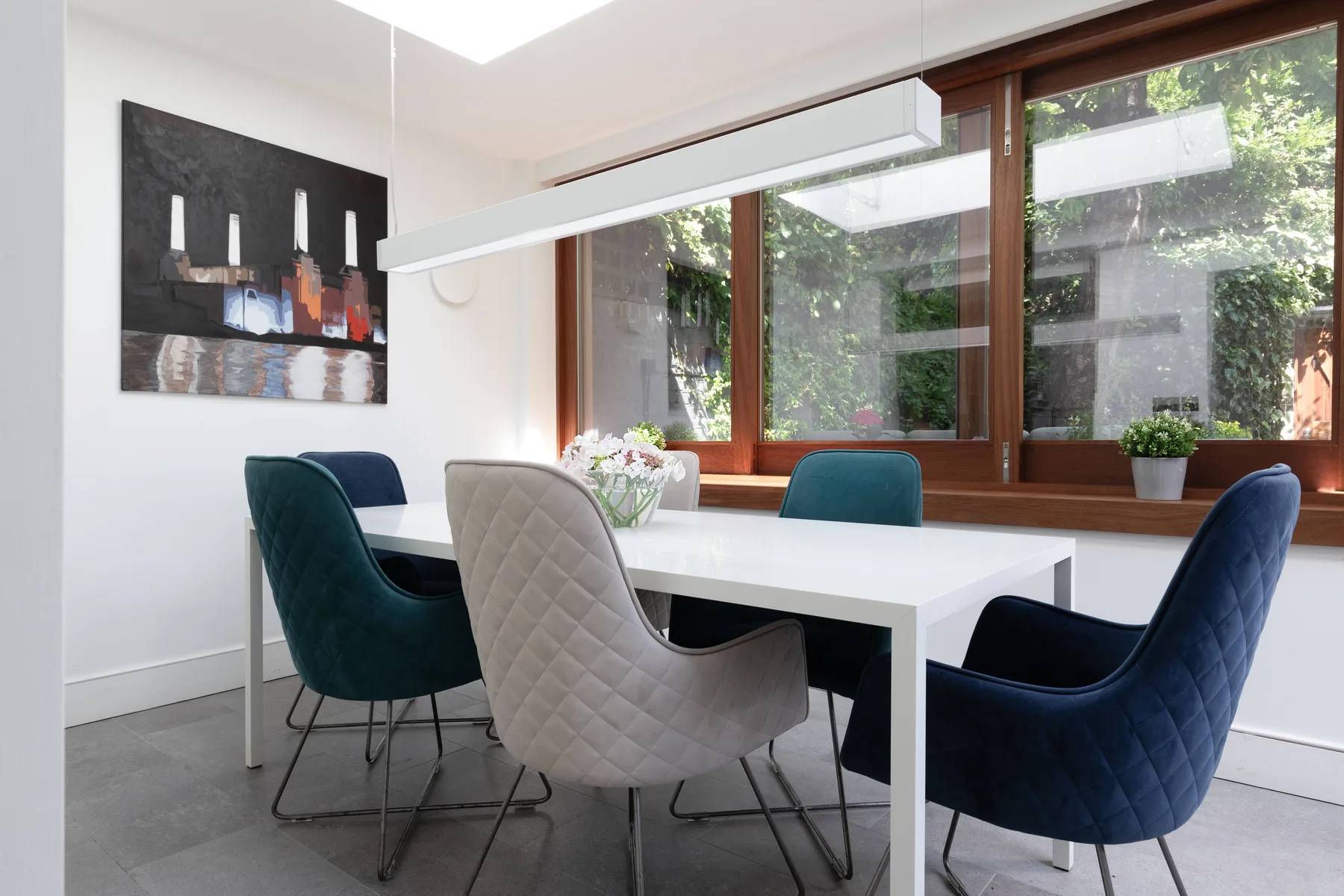A dining area with a white table and upholstered seating beside large windows.