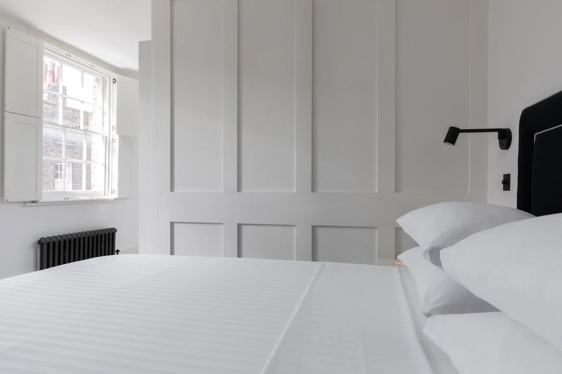 A bright bedroom with a neatly made bed beside a window.