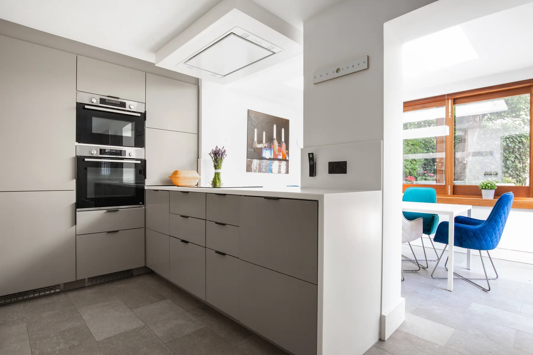 A modern kitchen with gray cabinets opens onto a dining area with blue seating.