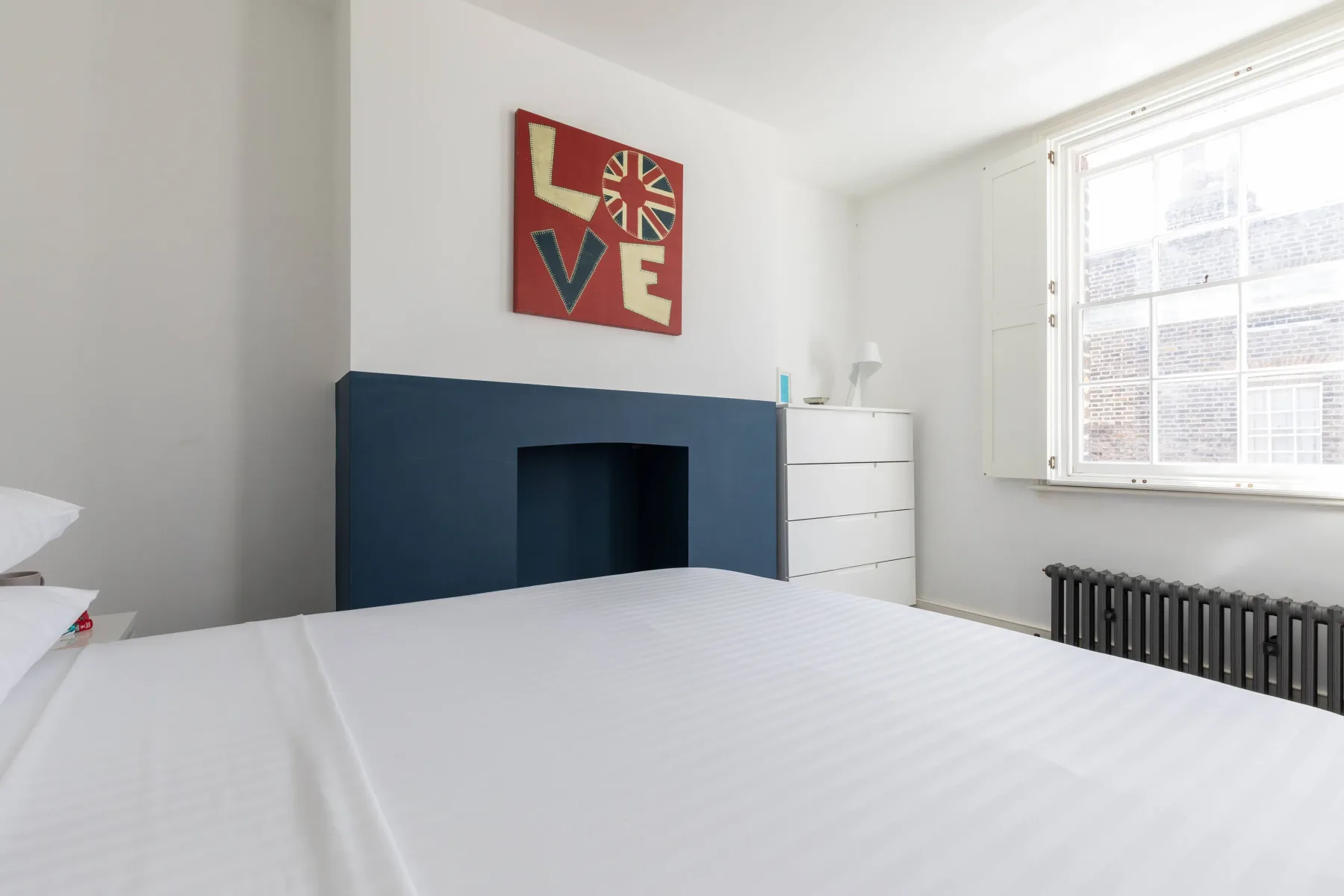 A bright bedroom with a bed, blue fireplace surround, and large window.