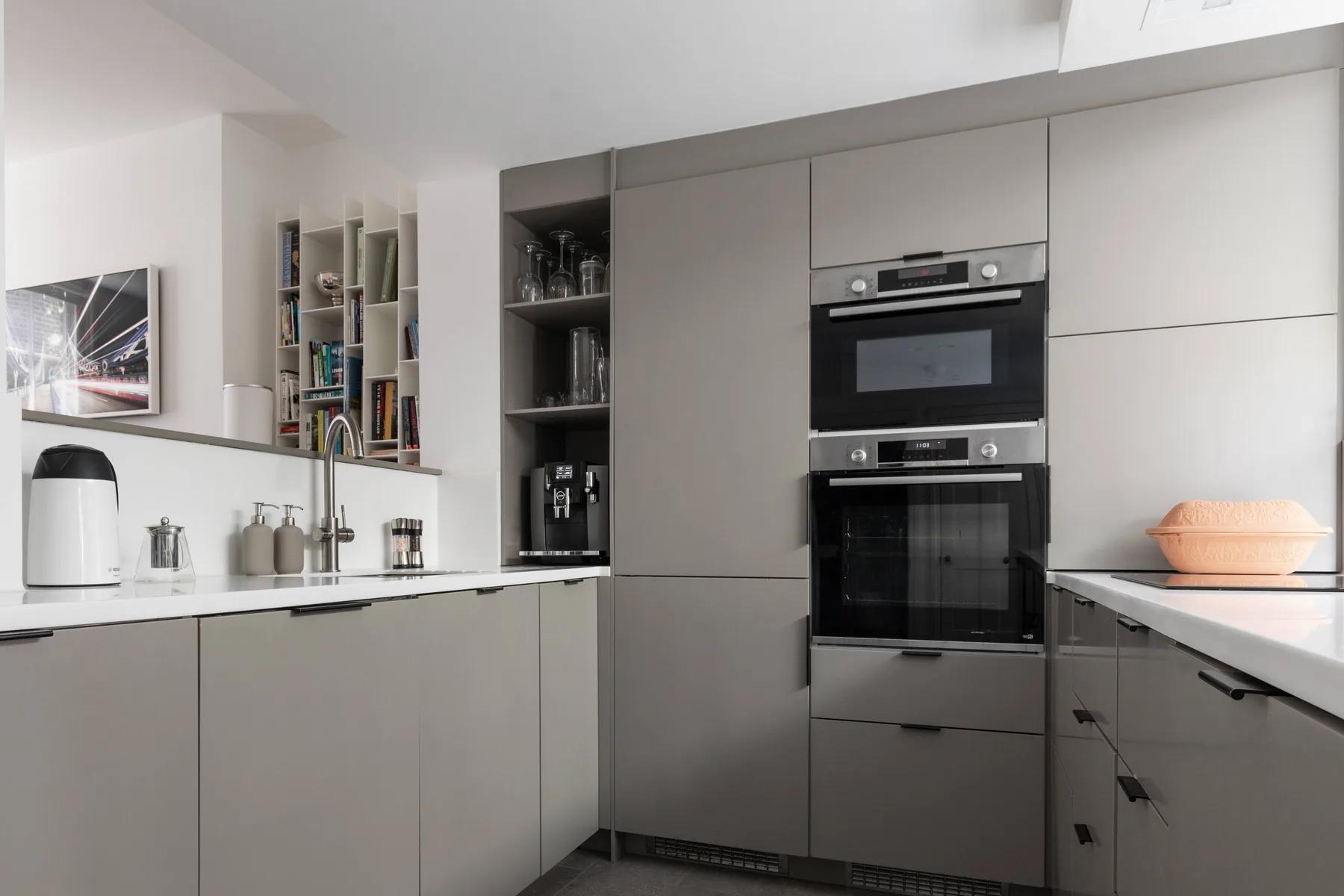 A modern kitchen with built-in ovens, gray cabinets, and a counter.