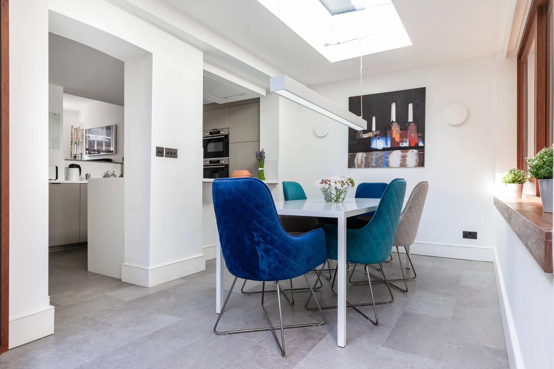 A bright dining area with a table, colorful seating, and a skylight.