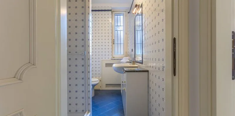 Un baño estrecho con paredes de azulejos estampados, un lavabo y una ventana.