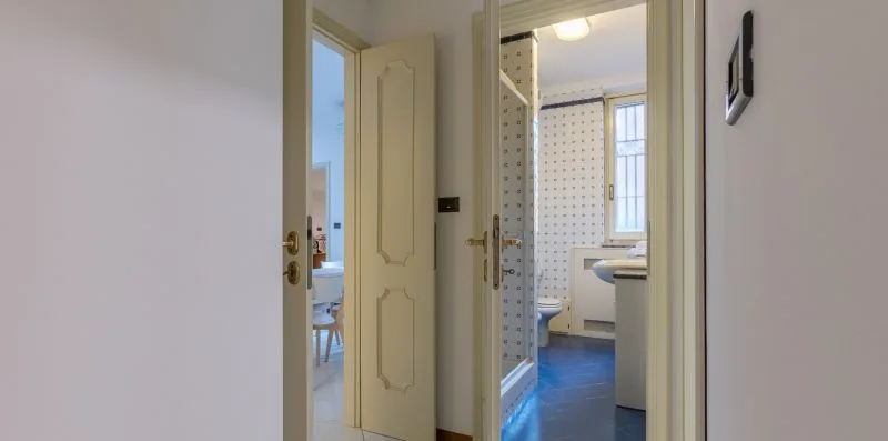 Vista de un pasillo a través de puertas abiertas hacia un baño con lavabo y ducha.