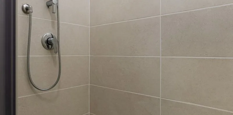 Una zona de ducha con azulejos, una ducha de mano y controles en la pared.