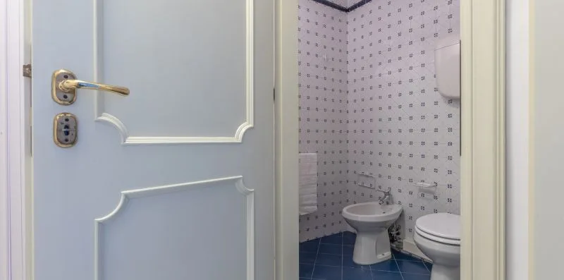 Un baño con bidé e inodoro junto a una puerta parcialmente abierta.