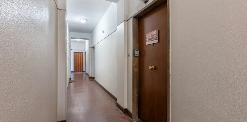 Un pasillo estrecho con una puerta marrón y una luz brillante en el techo.