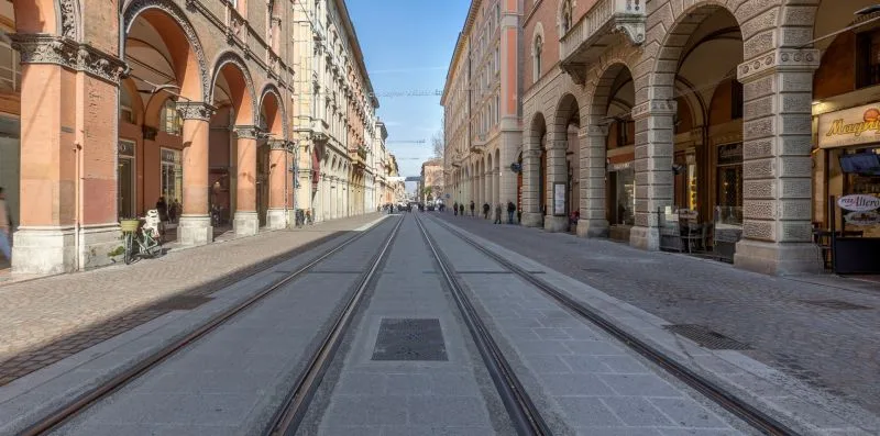 Una calle adoquinada con vías de tranvía discurre entre edificios con soportales.