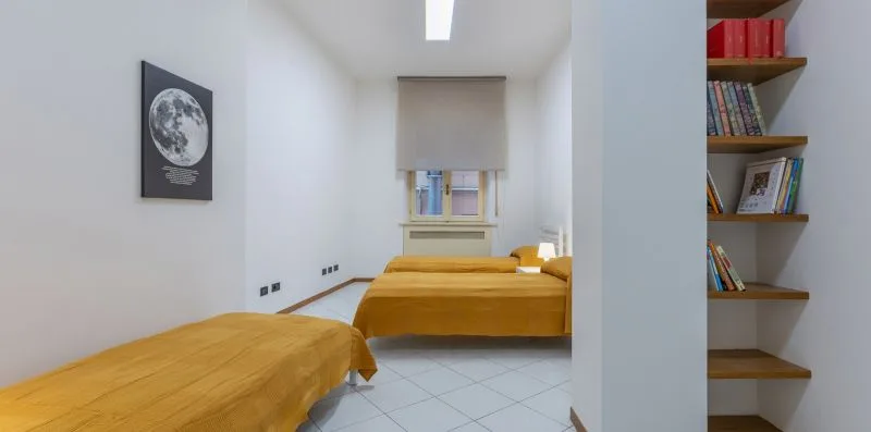 Un dormitorio luminoso con camas cubiertas de ropa de cama color mostaza y una ventana.