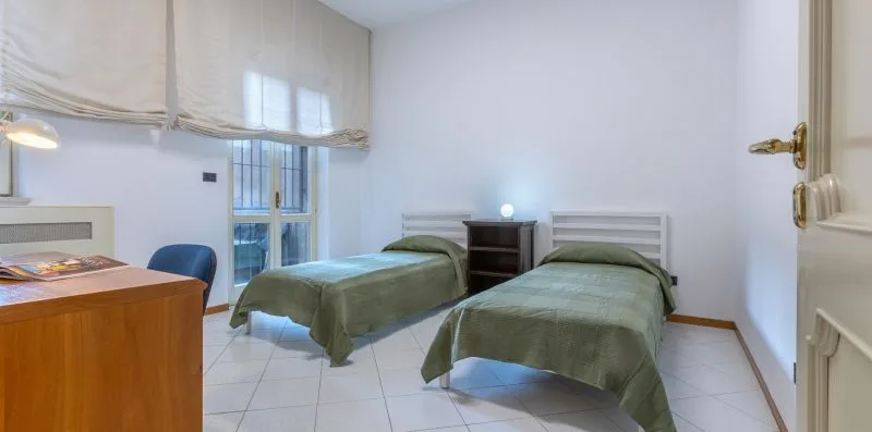 Un dormitorio luminoso con dos camas individuales, ropa de cama verde y una ventana.
