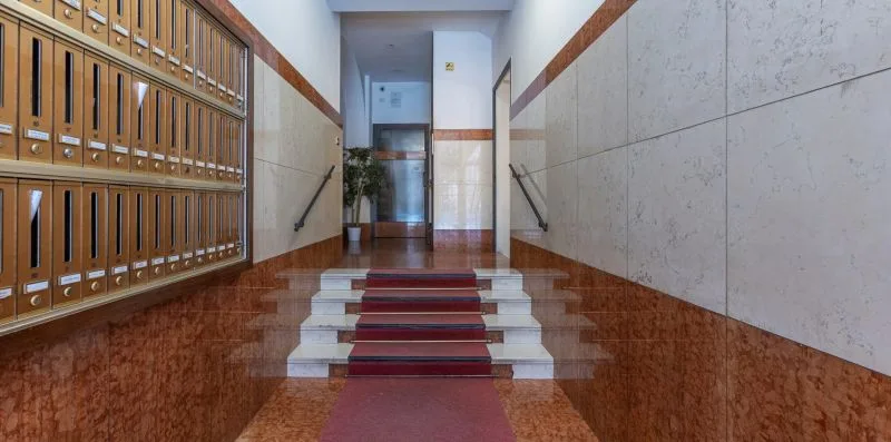 Un pasillo interior con buzones en una pared y escalones al fondo.