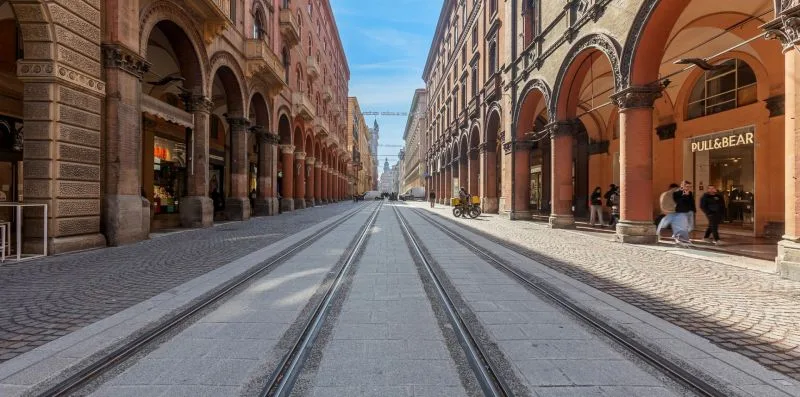 A city street lined with arcaded buildings, with tram tracks running through the center.
