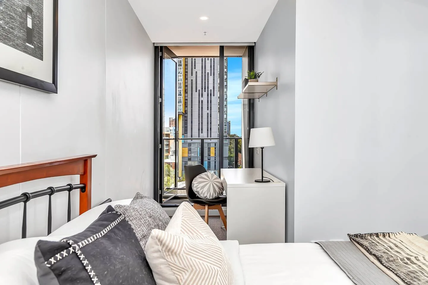 A bedroom with a bed and a small desk beside a large window.