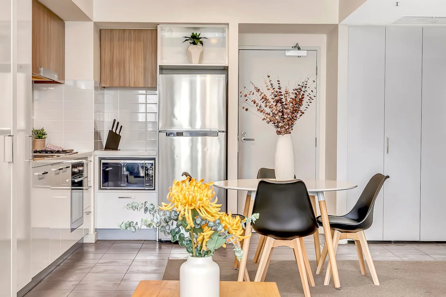A bright kitchen and dining area with a table, chairs, and a flower arrangement.