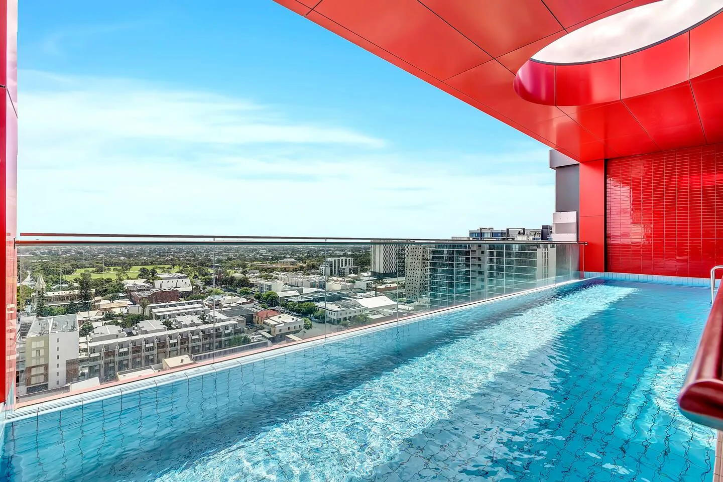 A rooftop pool with a glass railing overlooks the surrounding city.