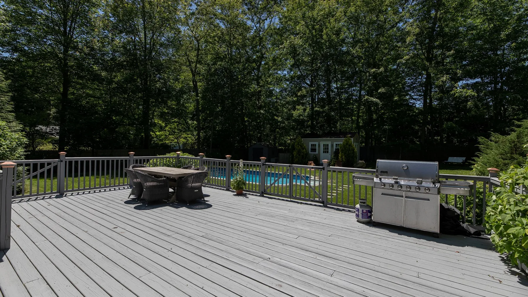 Una amplia terraza exterior da a una piscina, con una mesa y una parrilla cerca.