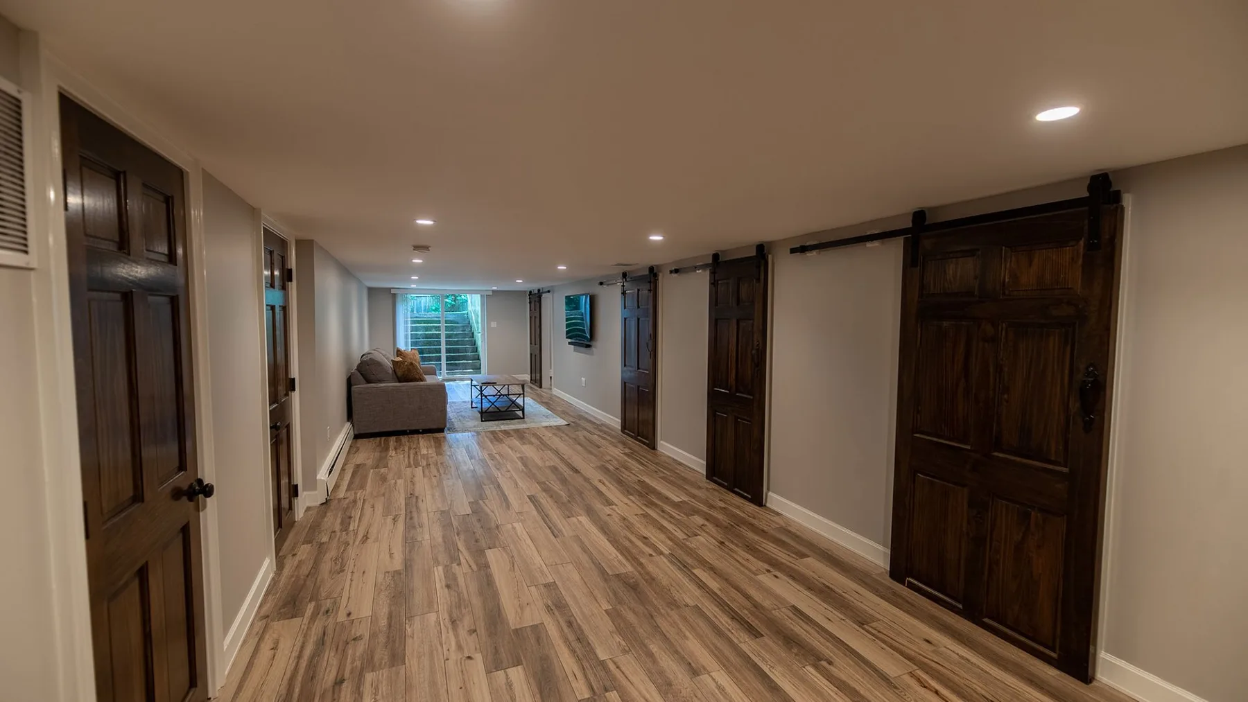 Un largo pasillo interior con piso de aspecto madera y varias puertas oscuras.