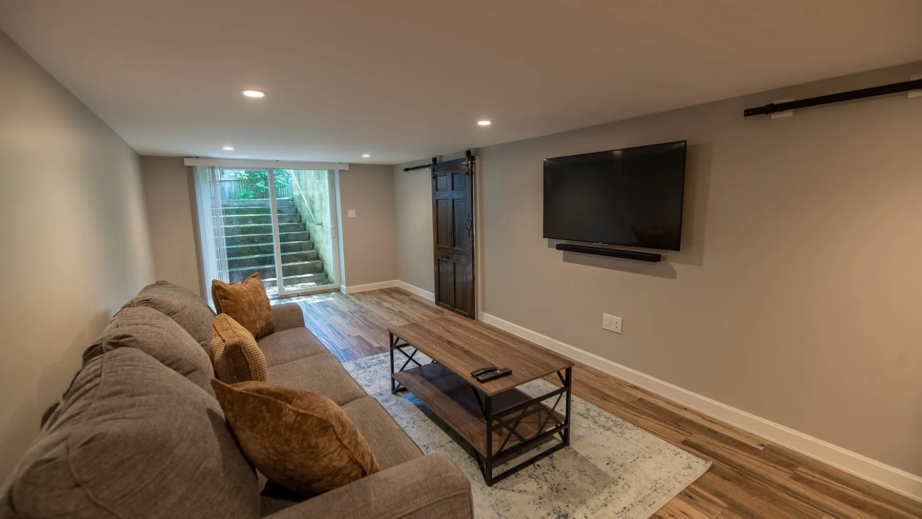 Una sala de estar con sofá seccional, mesa de centro y televisor en la pared.