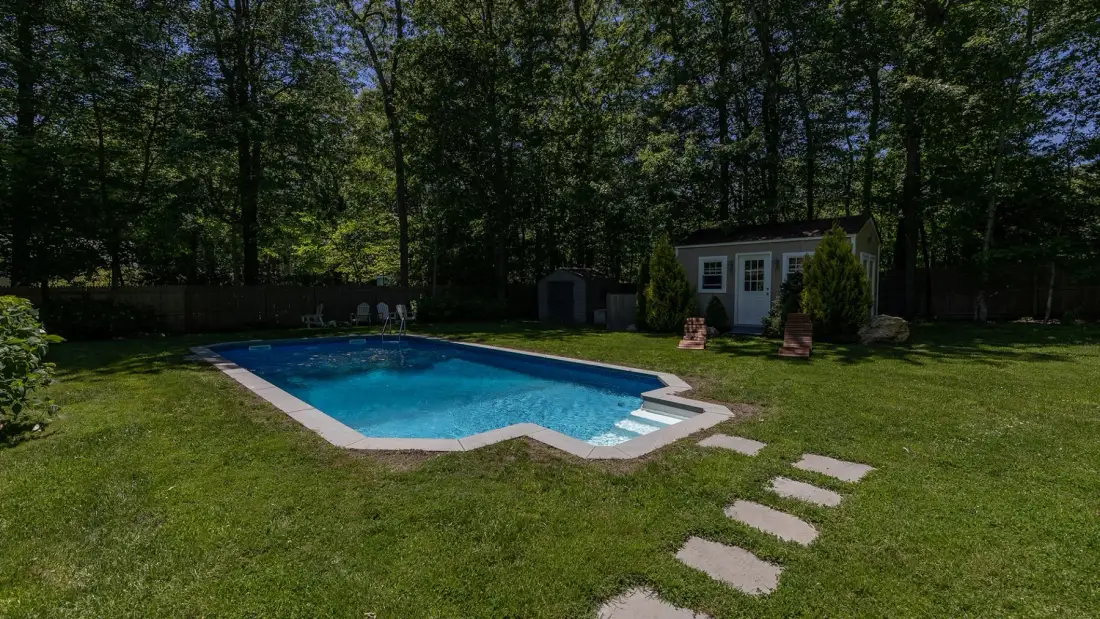 Una piscina al aire libre está en un jardín con césped rodeado de árboles.