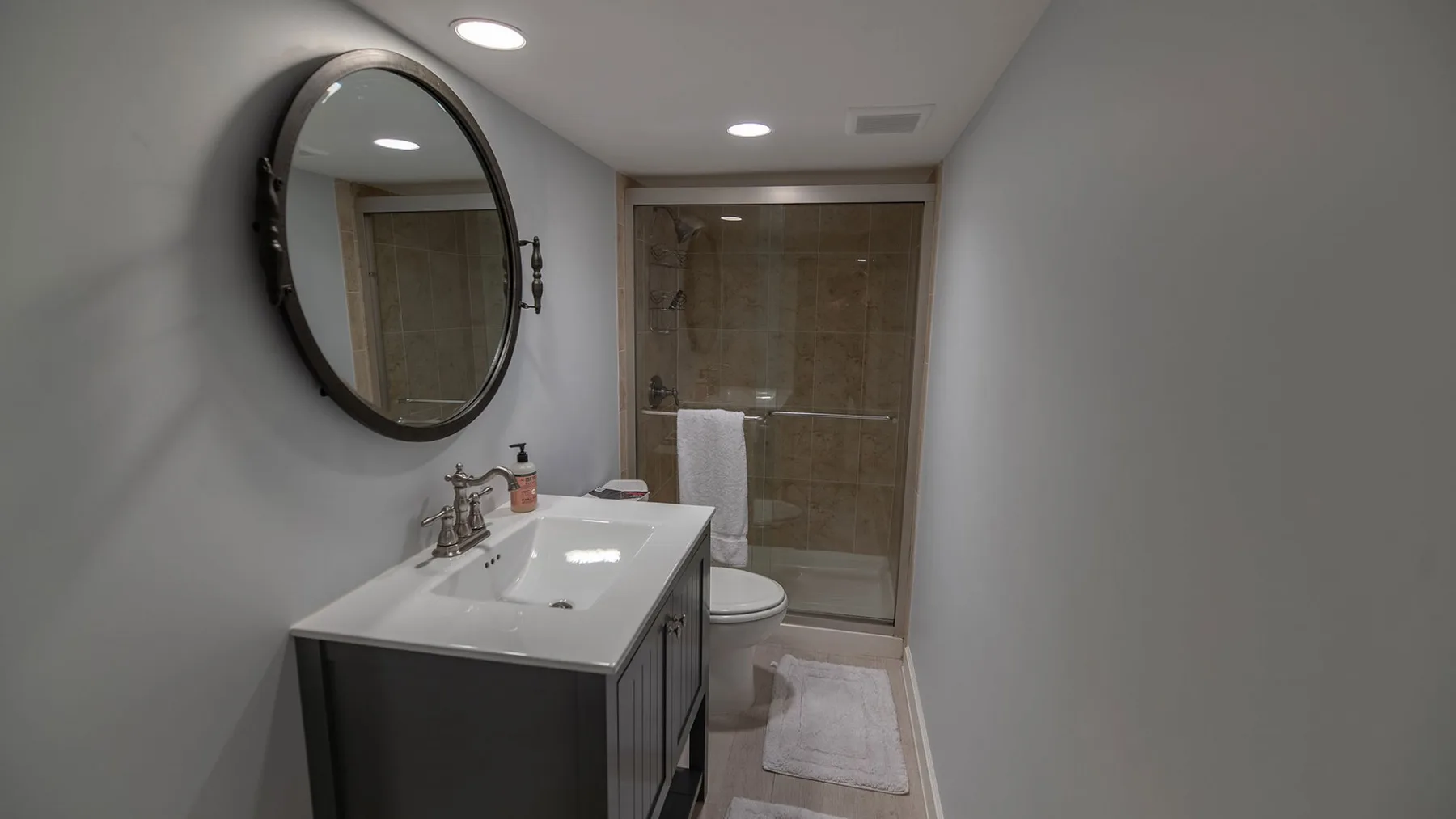 Un baño con lavabo, espejo redondo, inodoro y ducha de vidrio.