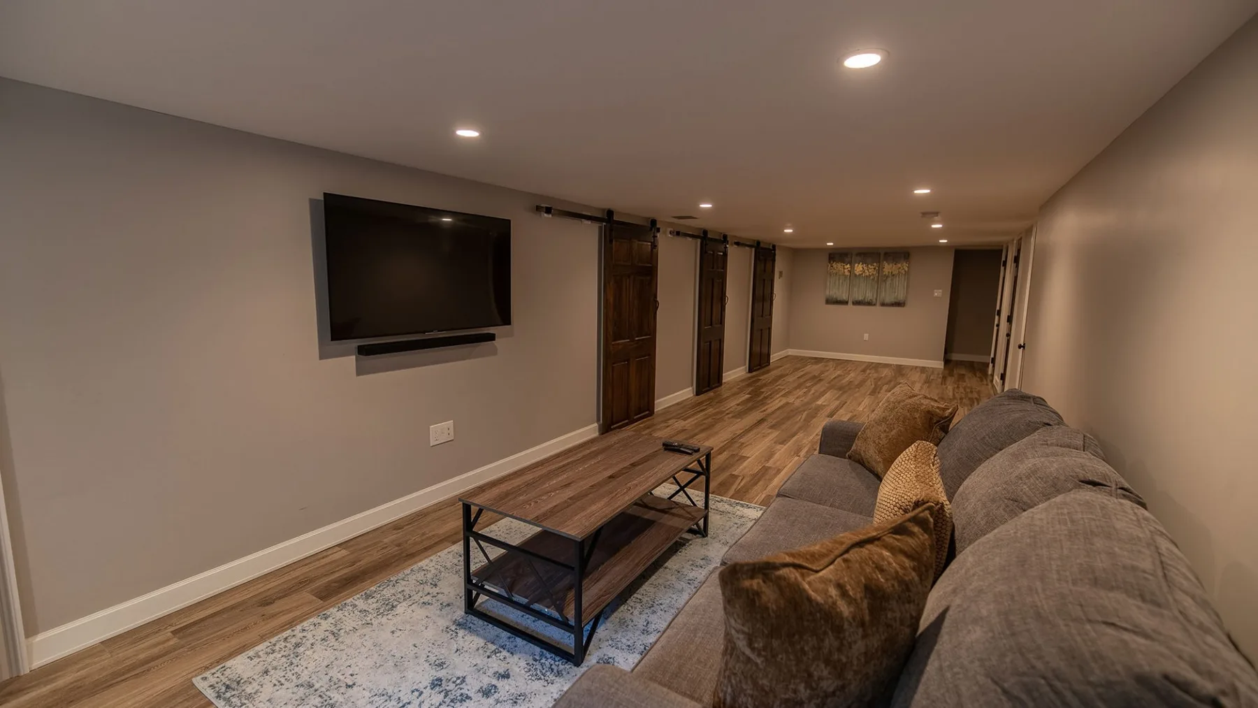 Una sala de estar en el sótano con asientos, una mesa de centro y un televisor en la pared.