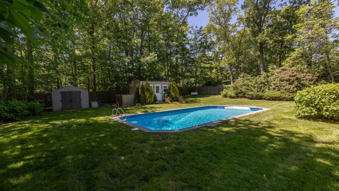 Una piscina está en un jardín con césped, rodeada de árboles.