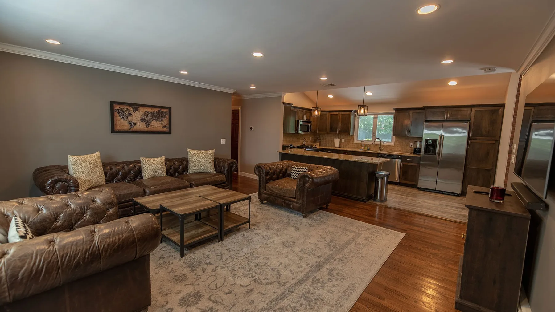 A living room with leather seating opens onto a kitchen with a central island.